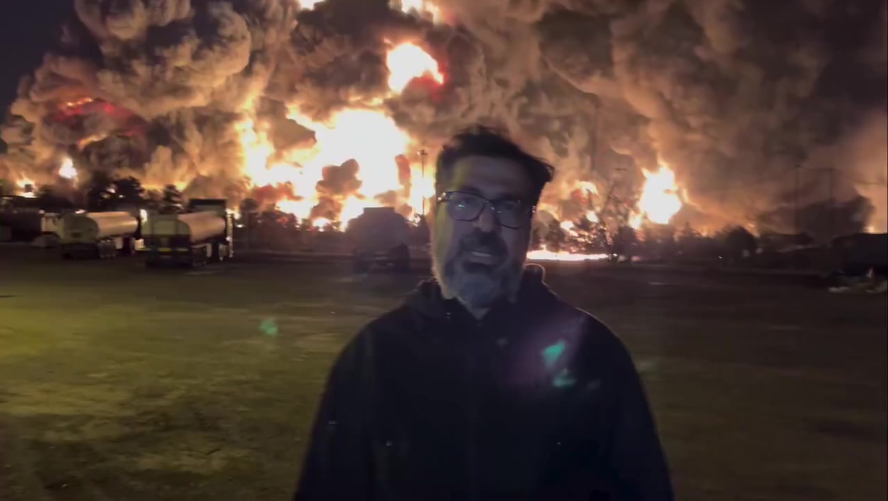 An Iranian journalist reports in front of the burning...